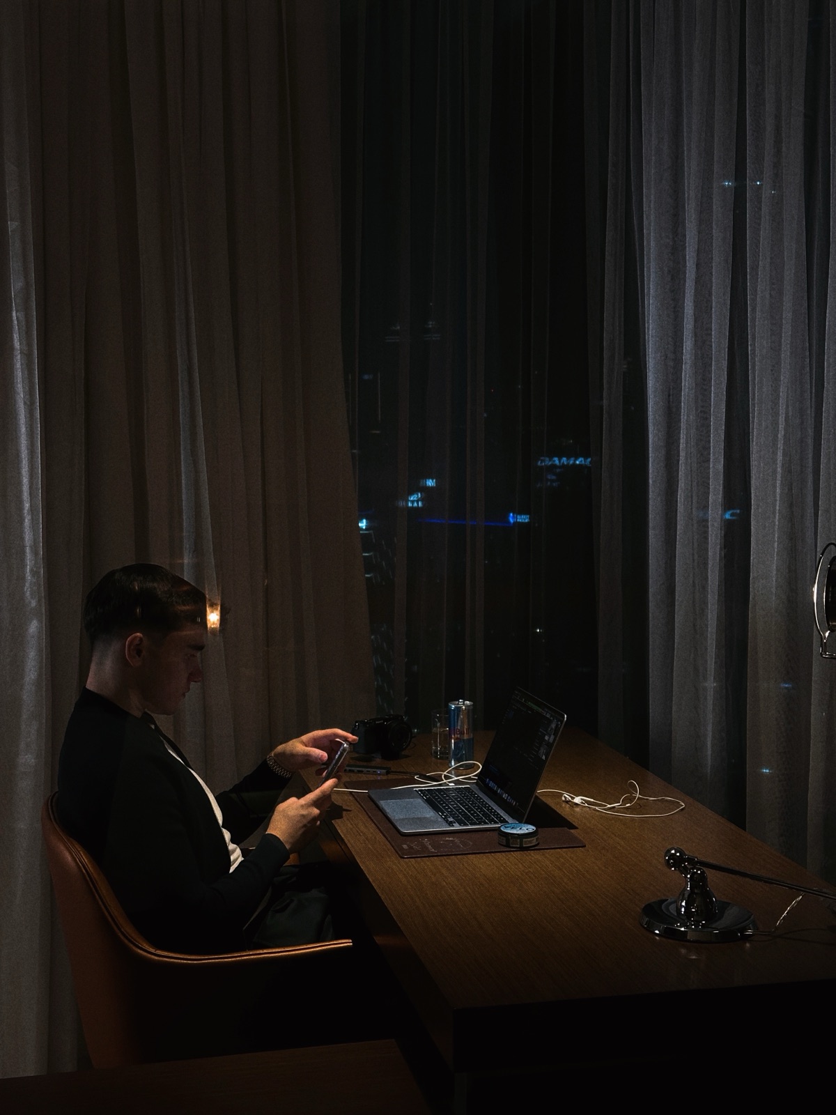 Danil arbeitet nachts am Schreibtisch — Dubai-Skyline durch den Vorhang